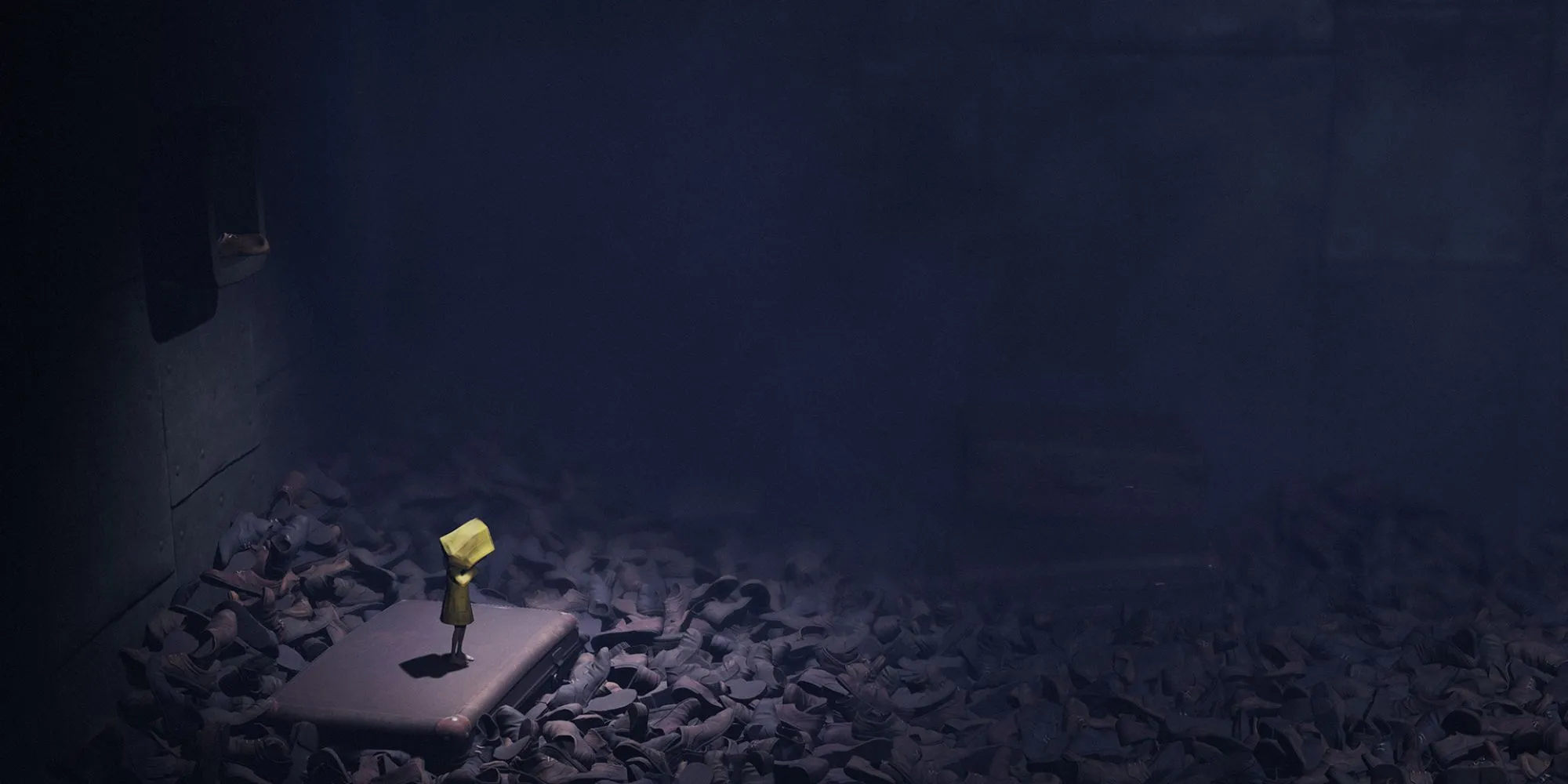 Six, nhân vật chính của Little Nightmares, đang đứng giữa những đống giày khổng lồ trong một căn phòng thiếu ánh sáng.